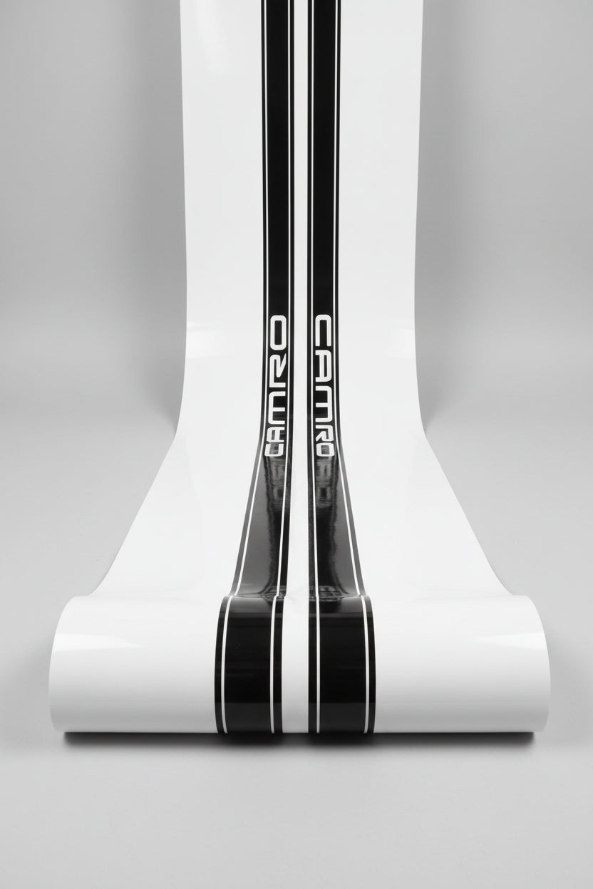 A close-up of a white surface with two vertical black stripes containing the word 'CAMARO' in white lettering, photographed in white studio