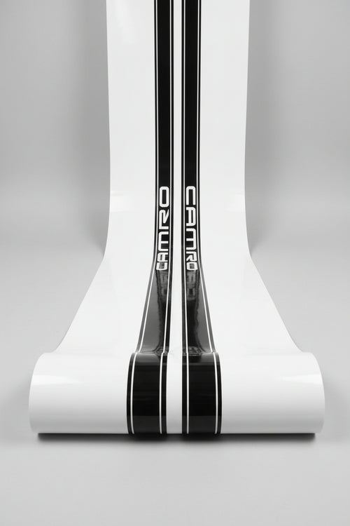 A close-up of a white surface with two vertical black stripes containing the word 'CAMARO' in white lettering, photographed in white studio